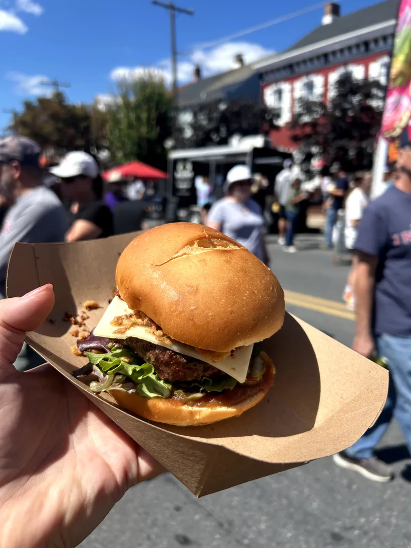 A festival cheeseburger — griddled patty, cheese, and crispy onions on a toasted bun — held up on a downtown Hamburg street.